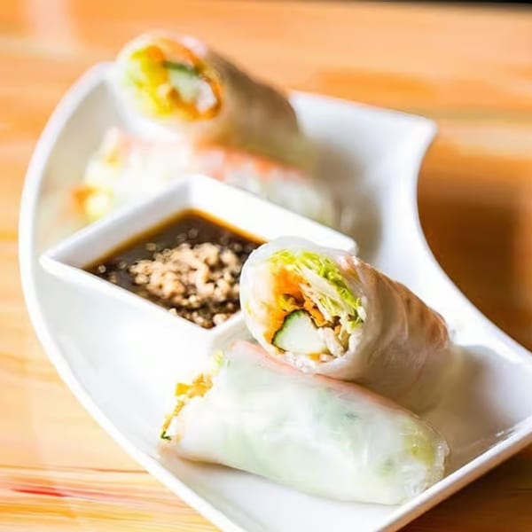 Fresh Thai spring rolls with shrimp, vegetables, and peanut dipping sauce on a white plate.