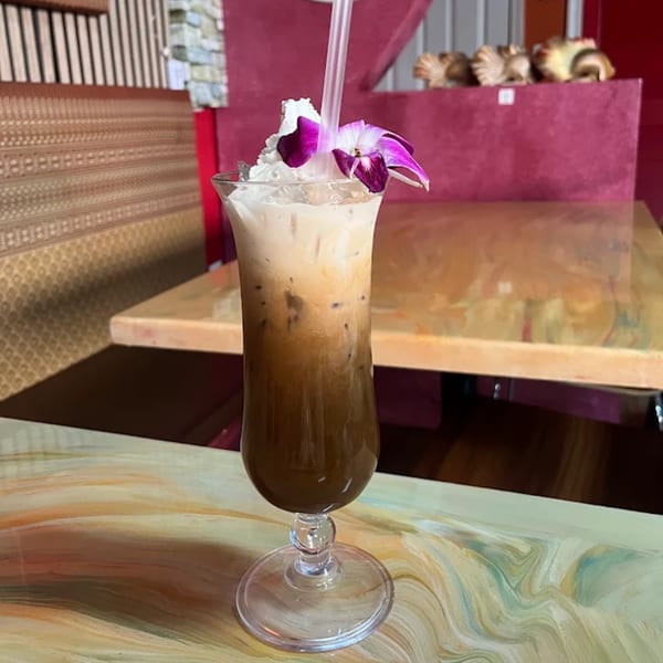 Iced Thai coffee with whipped cream and an orchid garnish on a marbled table at Nisa Thai.