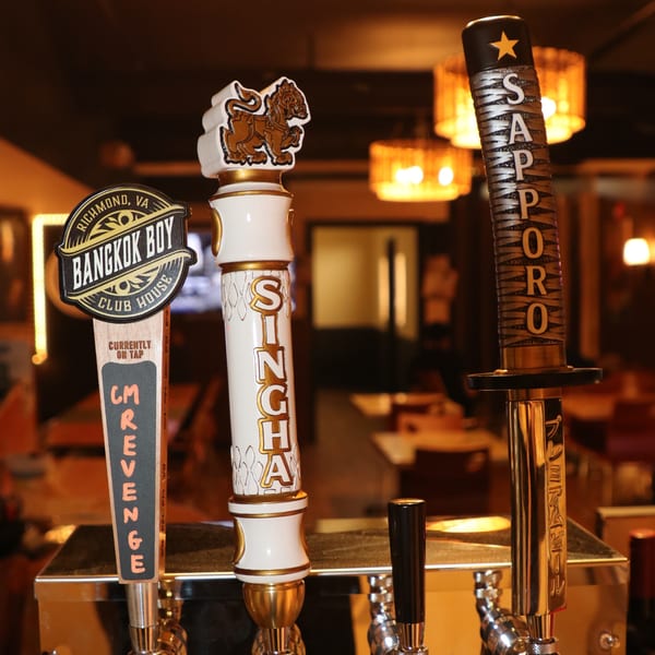 Three beer taps, including Bangkok Boy, Singha, and Sapporo, on a bar with warm lighting.