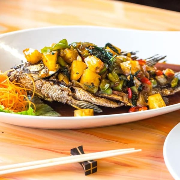 Whole fried fish topped with pineapple, bell peppers, and sauce, served with chopsticks.