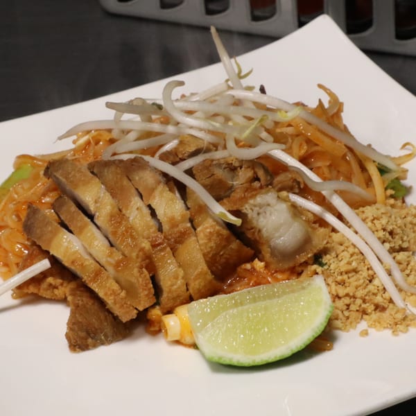 Pad Thai with sliced crispy pork belly, bean sprouts, crushed peanuts, and a lime wedge.