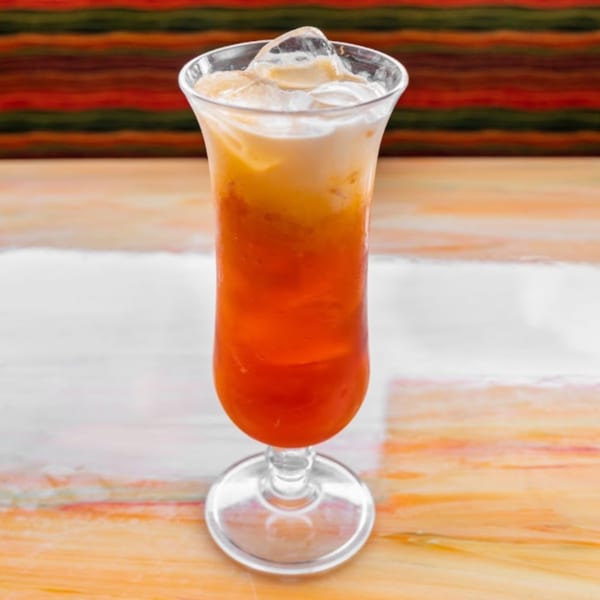 A tall glass of Nisa Thai Iced Tea with ice, showing distinct orange and white layers.