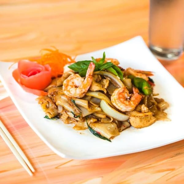 Nisa Thai Asian Cuisine's Pad See Ew with shrimp, onions, and basil, garnished with a tomato rose.